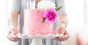 Person holding pink cake and tray with bright purple dahlia