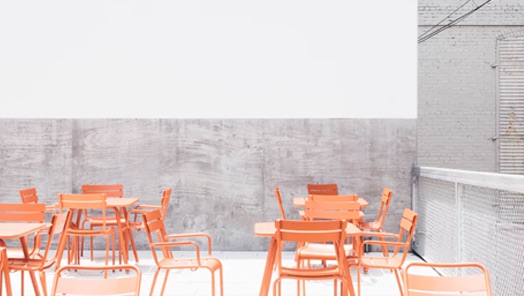 view of brightly lit concrete-walled restaurant with orange tables and chairs